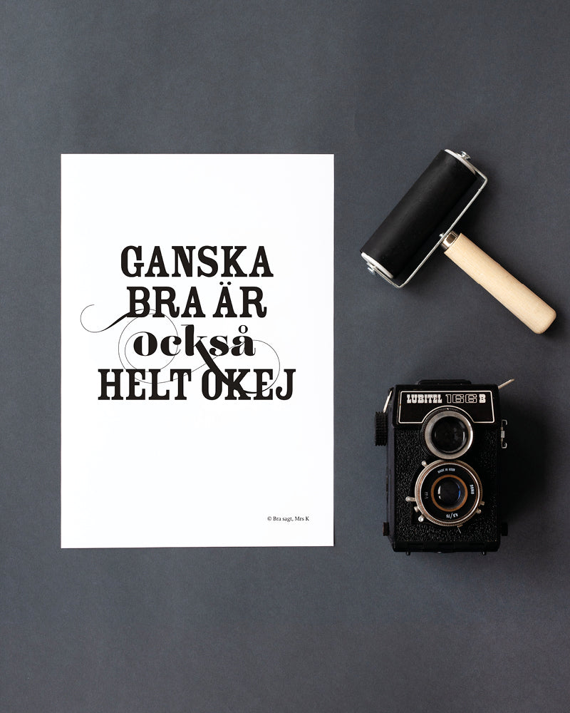 Poster med svenska citatet "Ganska bra är också helt okej" placerat på grå yta.