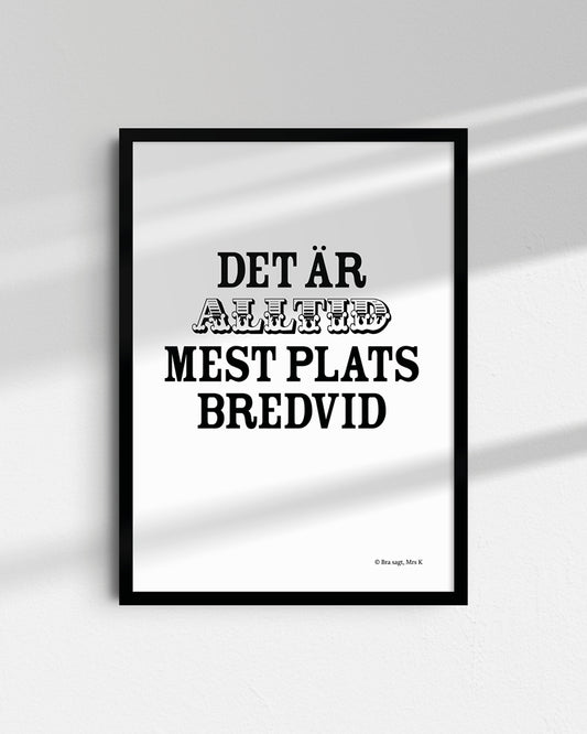 Poster med svenska citatet "Det är alltid mest plats bredvid" i ram på vägg.