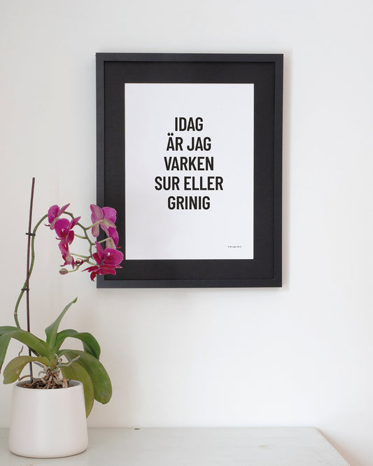 Poster med svenska citatet "Idag är jag varken sur eller grinig" på vägg vid bord.