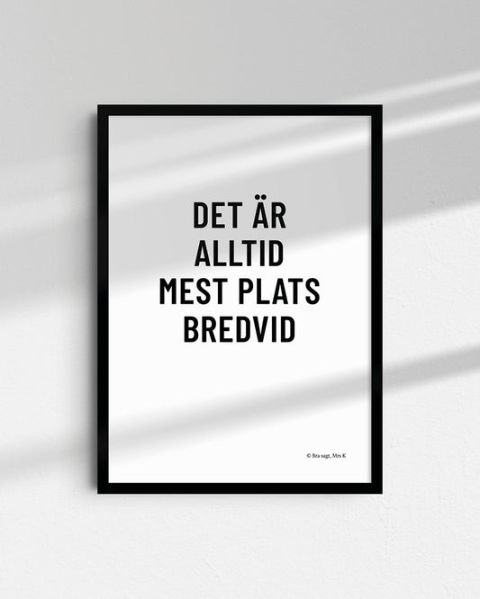 Poster med svenska citatet "det är alltid mest plats bredvid" i ram på vägg.