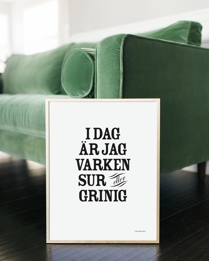 Poster med svenska citatet "Idag är jag varken sur eller grinig" i ram mot soffa. 