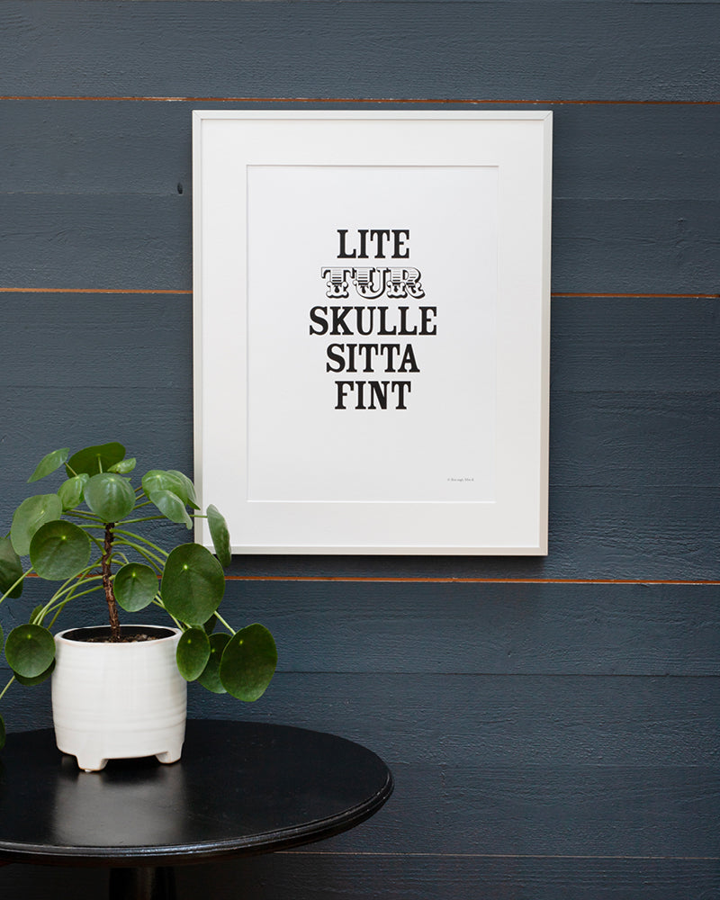 Poster med svenska citatet "Lite tur skulle sitta fint" i ram vid bord. 