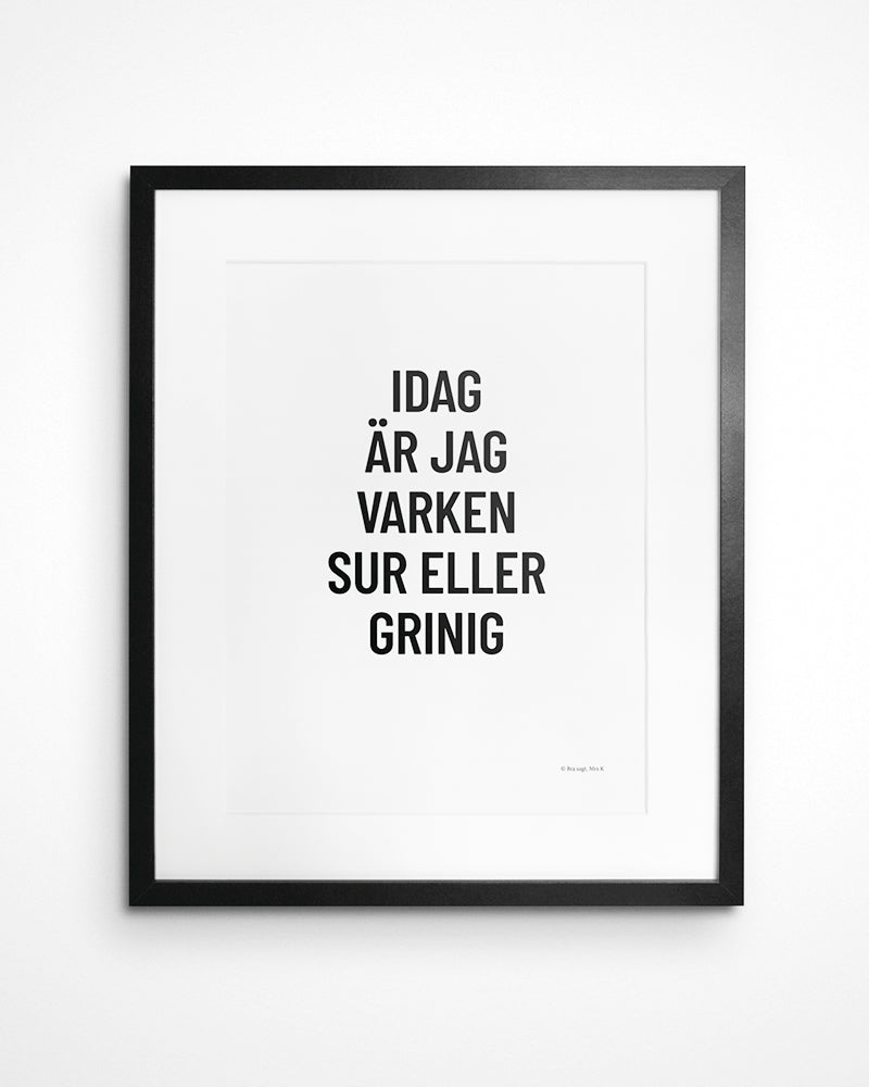 Poster med svenska citatet "Idag är jag varken sur eller grinig" i ram på vägg. 