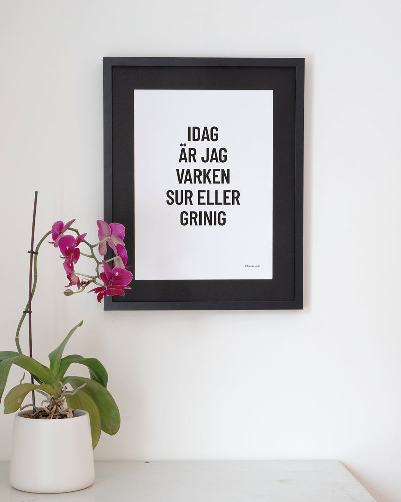 Poster med svenska citatet "Idag är jag varken sur eller grinig" på vägg vid bord. 